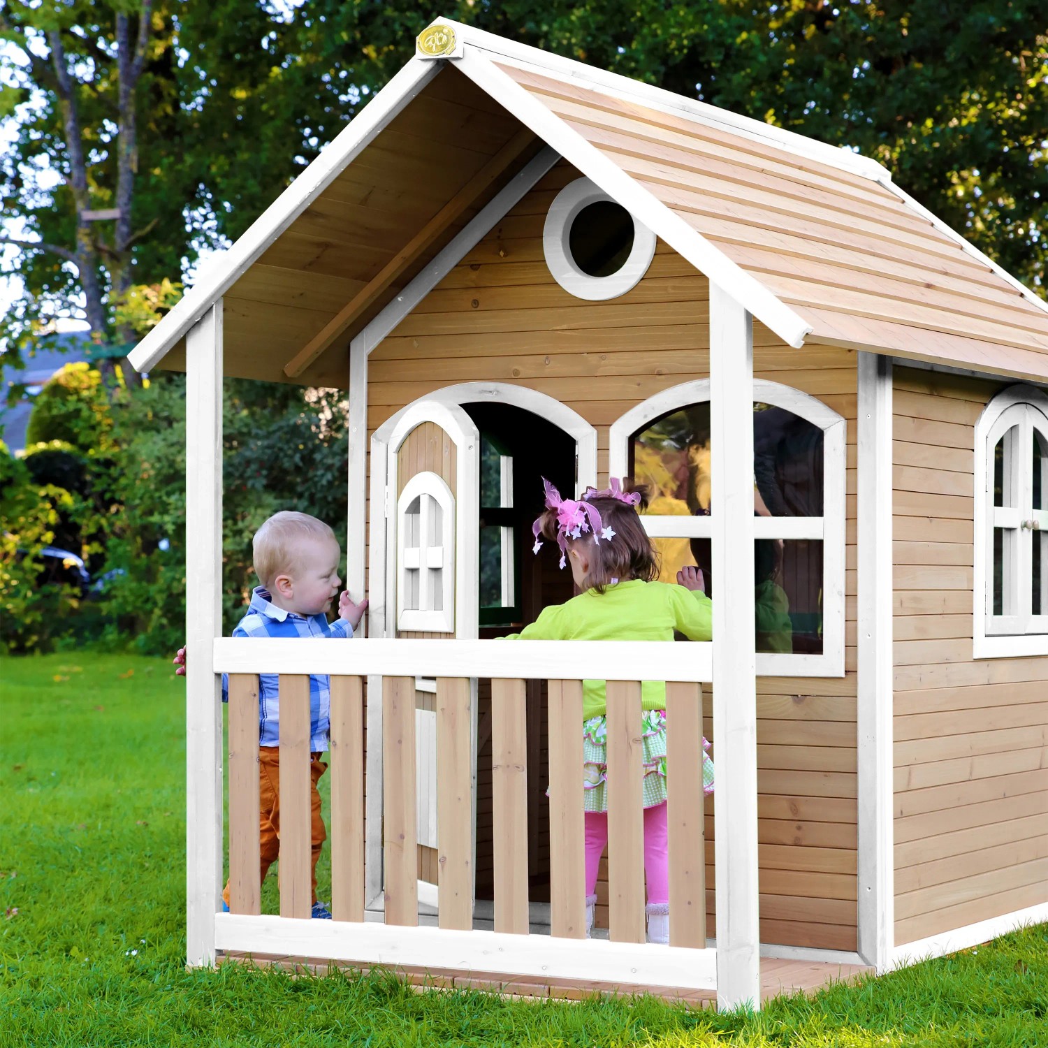 Axi Alex Spielhaus aus Holz in Braun/Weiß mit Veranda und zwei spielenden Kindern im Garten.