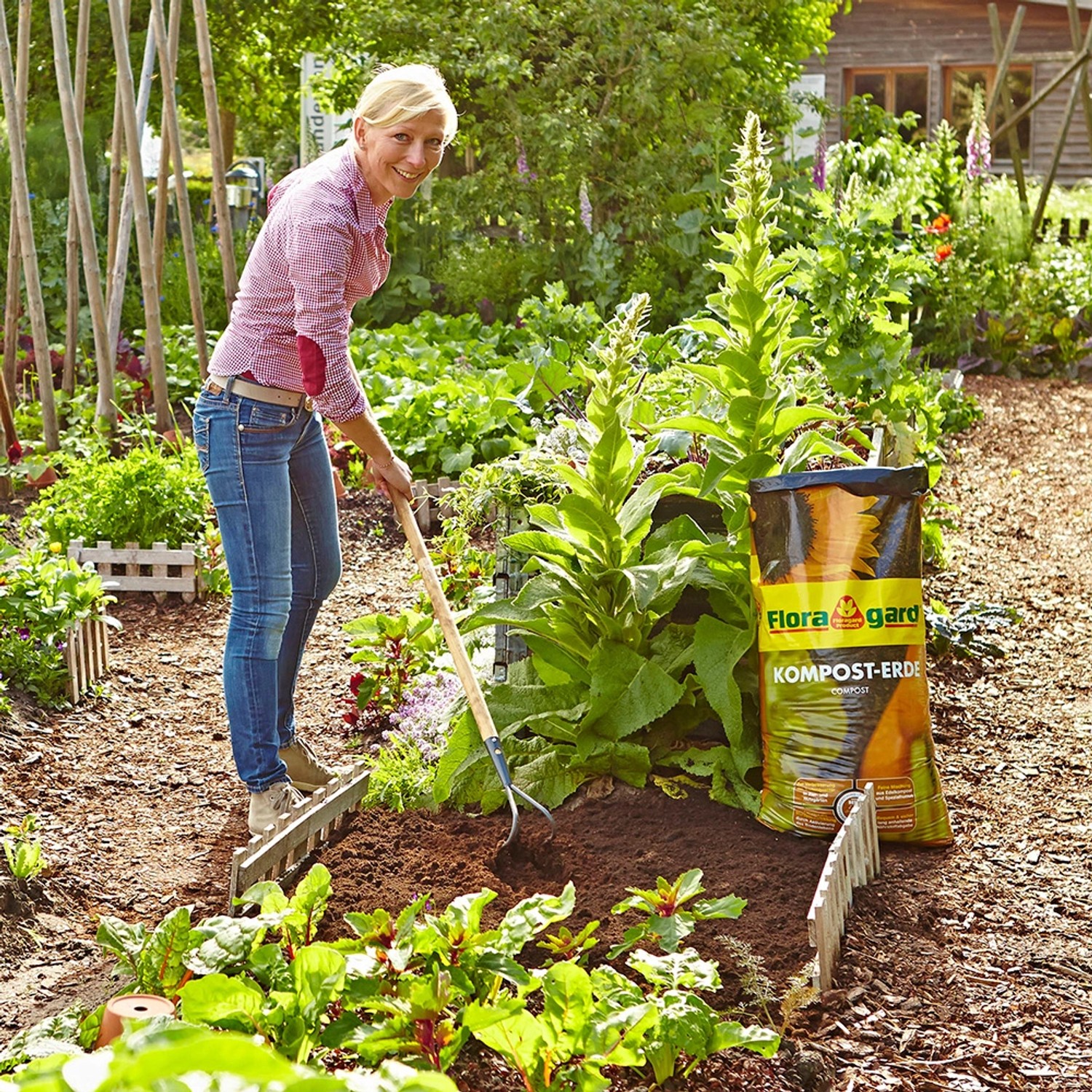 Frau arbeitet mit Floragard Bio-Kompost-Erde im Garten. Sack Hochbeeterde im Hintergrund.