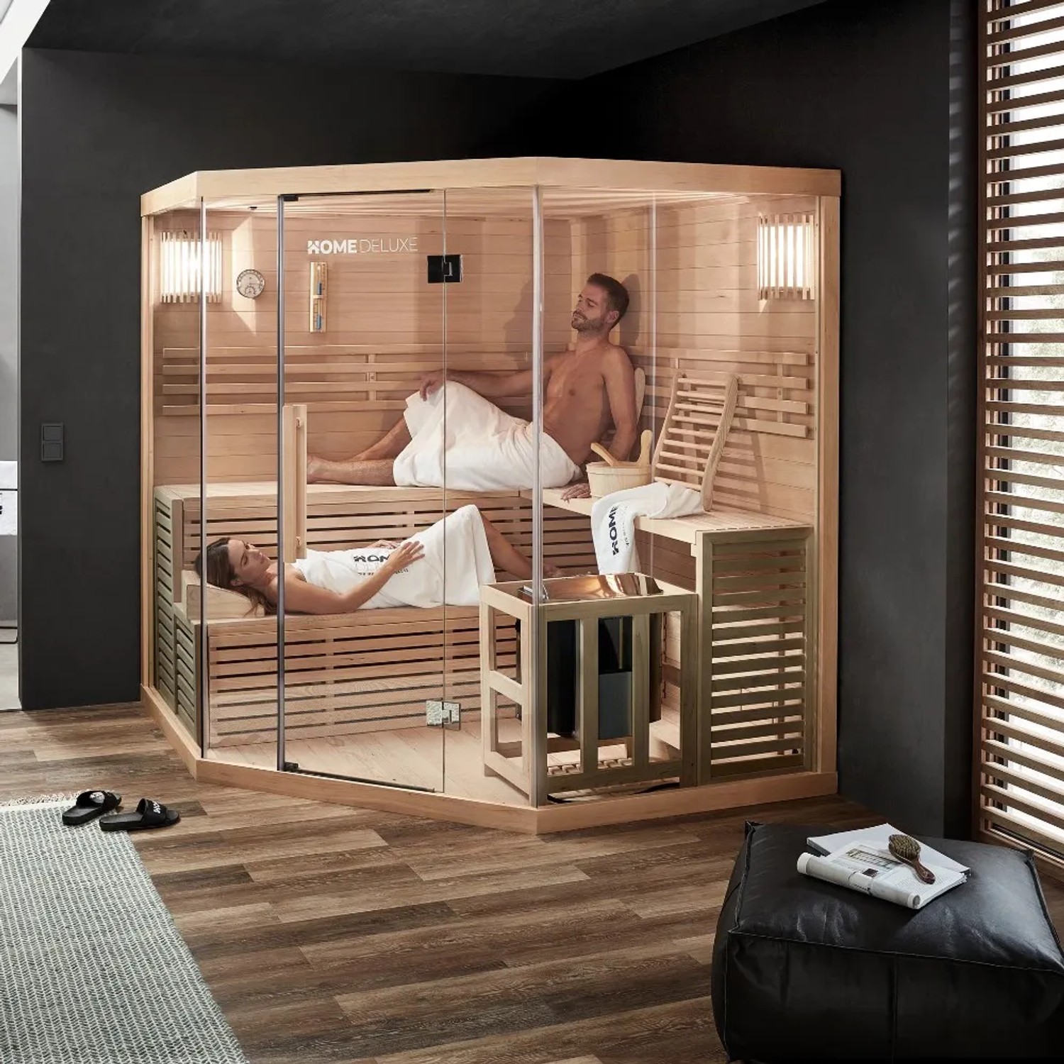 Große, helle Sauna SKYLINE BIG aus Tannenholz mit Glasfront und zwei Personen auf den Bänken.