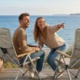 Lachendes Paar in beigen osoltus Faltsesseln mit Holzlehnen am Meer. Verstellbarer Campingstuhl aus Aluminium.