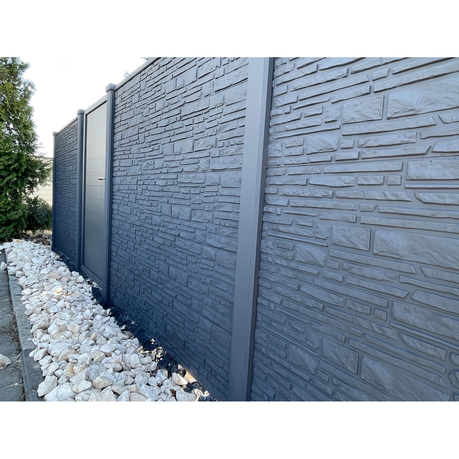 Graue Beckers Betonzaun Platte Klassik Montana als Sichtschutz mit Tür und Steinen im Garten.