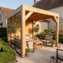 Moderne weka Gartenlaube Lumley aus Fichte mit Flachdach, Glas- und Holzwand auf Terrasse im Garten.