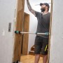 Mann installiert Holztürzarge mit zwei wolfcraft Türfutterstreben Easy. Die Spannwerkzeuge stabilisieren die Zarge beim Einbau.