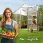 Lachende Gärtnerin mit Erntekorb vor transparentem Tectake Gewächshaus mit Alu-Rahmen, Schiebetür, Dachfenster.