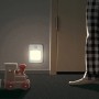 Warmweißes LED-Nachtlicht mit Bewegungsmelder an der Wand, daneben ein Spielzeugzug und eine Person.