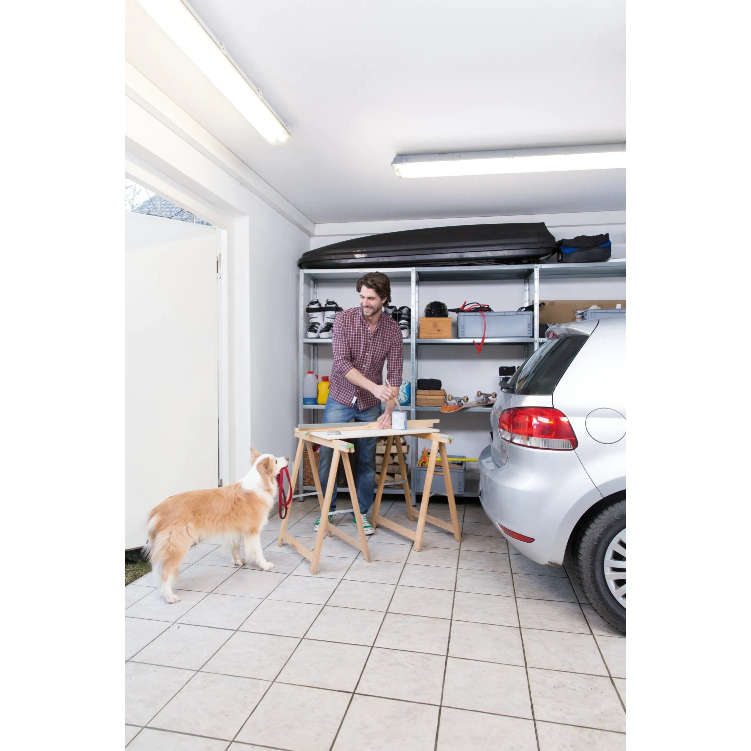 Mann arbeitet in Garage mit Ledvance LED-Feuchtraumleuchte. Werkstattbeleuchtung mit kaltweißem Licht.