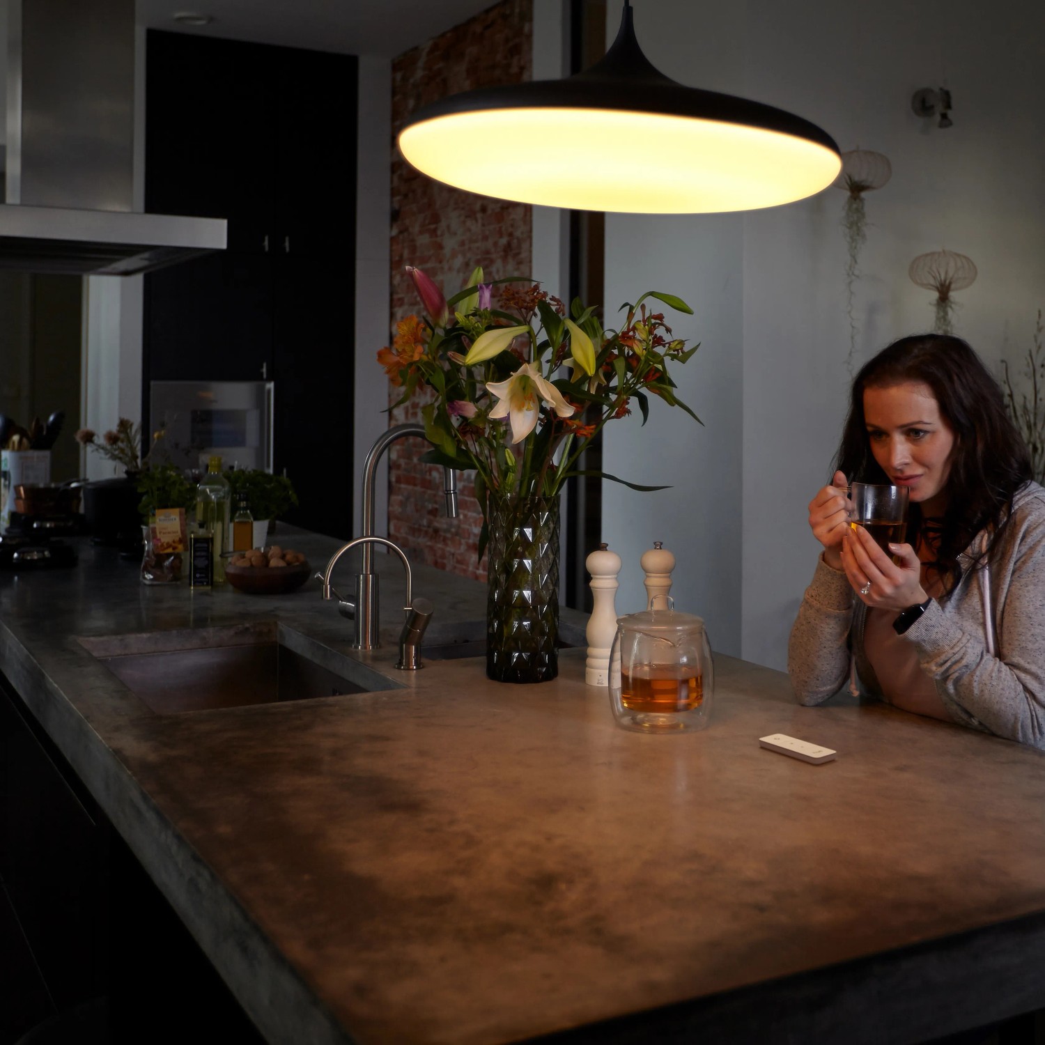 Frau mit Tasse unter Philips Hue Leuchte; Dimmschalter auf Küchentisch.