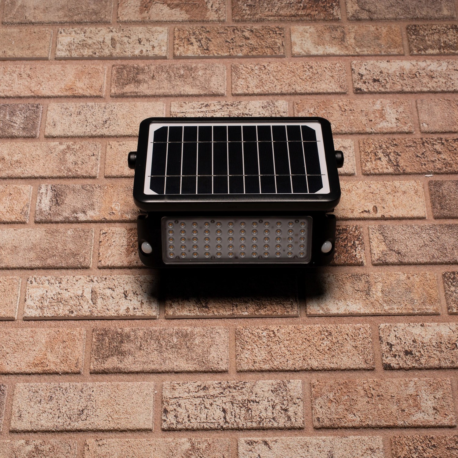Schwarze LED Solar-Außenleuchte mit Sensor und Flutlicht an einer Backsteinwand.