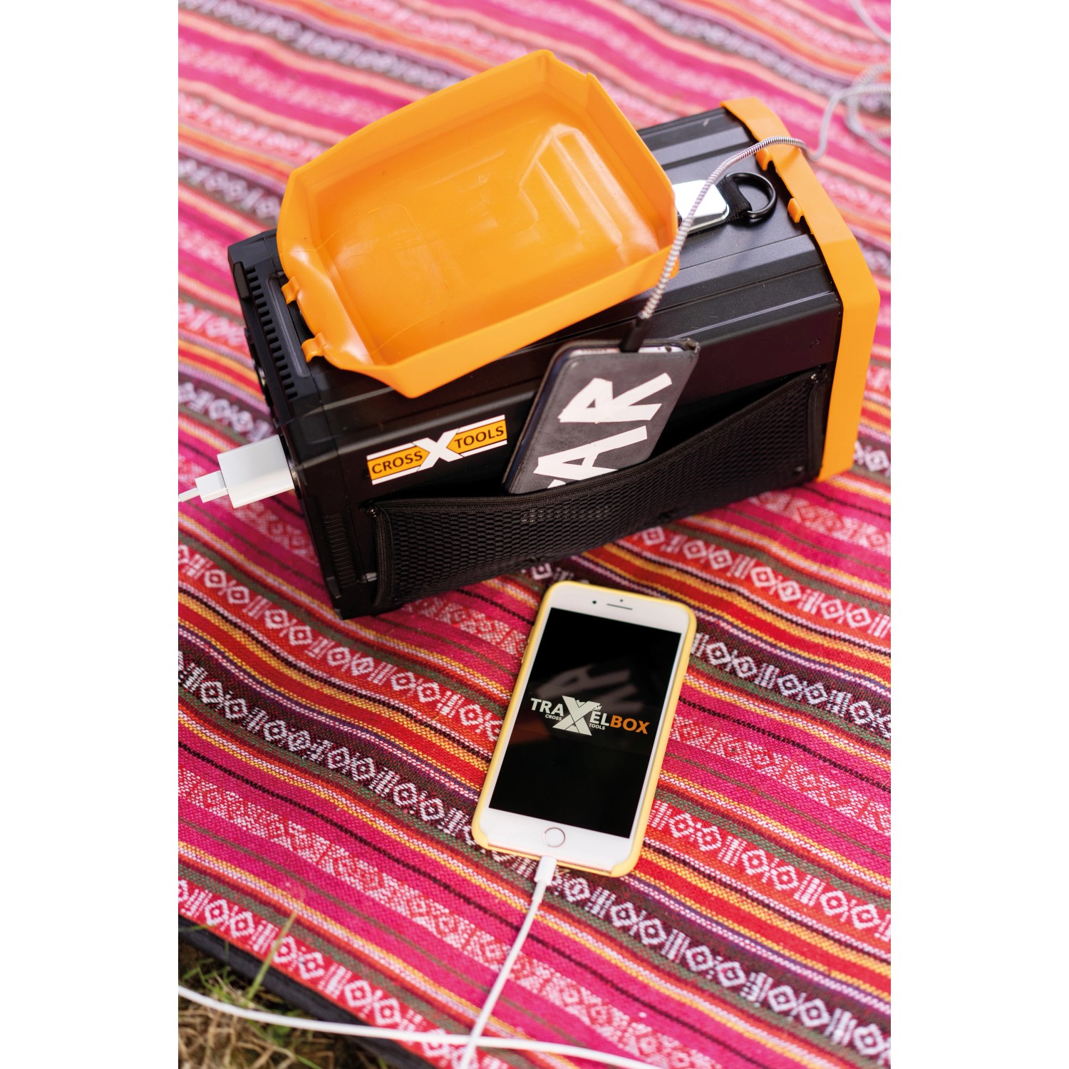 Cross Tools Travelbox 500+ Power Station mit Zubehör und geladenem Smartphone auf bunter Decke.