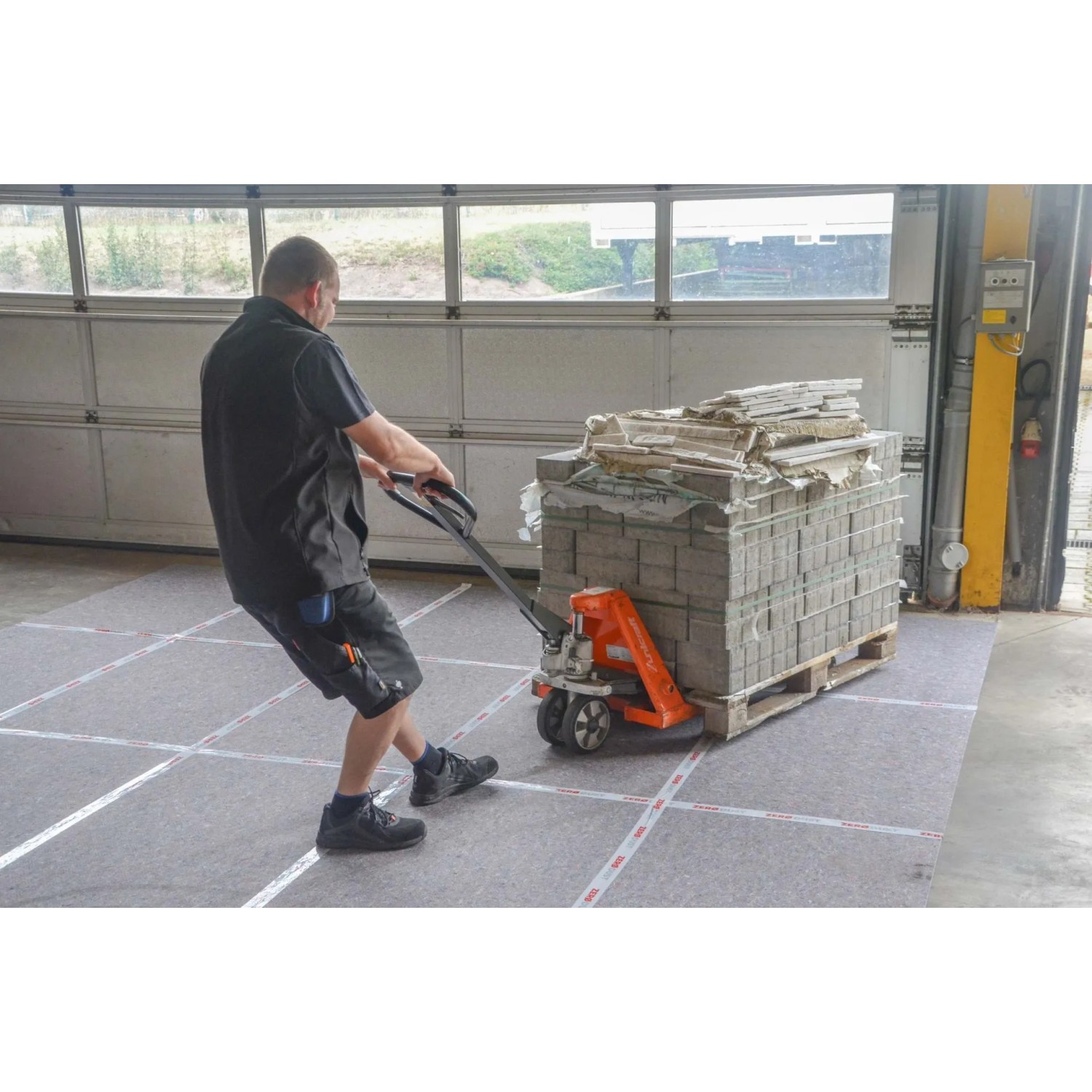 Mann zieht Palette mit Steinen auf Scorprotect Vliesfaserplatten zum Schutz des Bodens.
