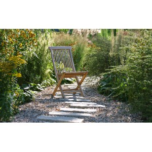Gartenstuhl aus Holz auf Kiesweg im Garten. Klappstuhl aus Holz vor üppiger Gartengestaltung.