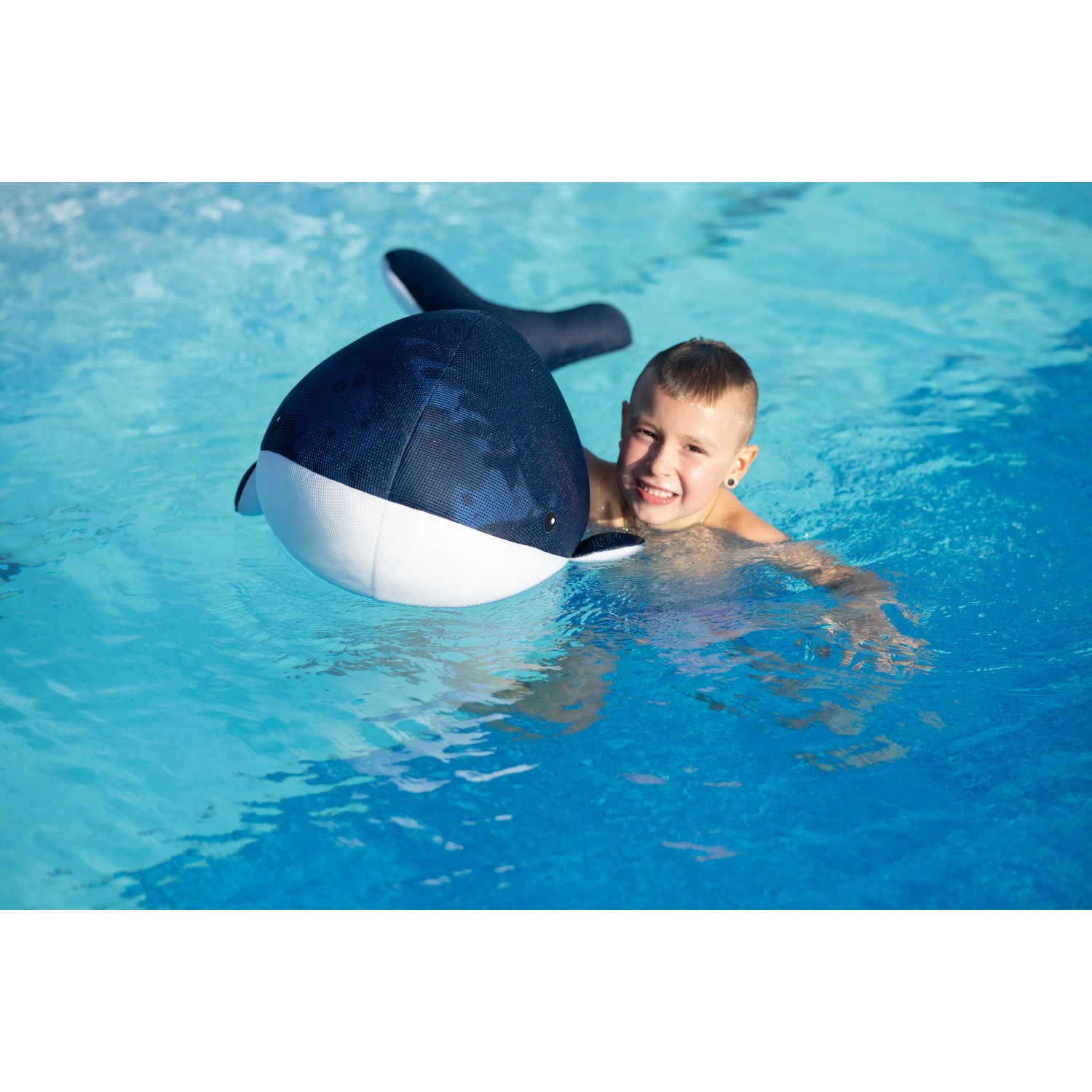 Junge schwimmt mit blau-weißem Westmann Pool Buddy Wal im Pool.