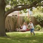 Rote Relaxdays Nestschaukel im Garten. Ein Mädchen sitzt, ein Junge schiebt die runde Schaukel.
