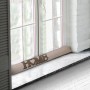 Beautissu Tuuli Zugluftstopper, 8x100cm, Natur, vor Fenster mit "HOME" Schriftzug.