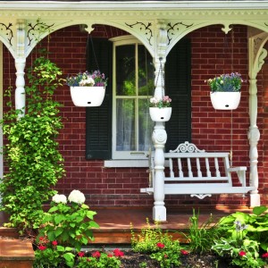 Drei weiße Kunststoff Blumenampeln mit Wasserspeicher hängen bepflanzt an einer Veranda. Ideal für Balkon & Garten.