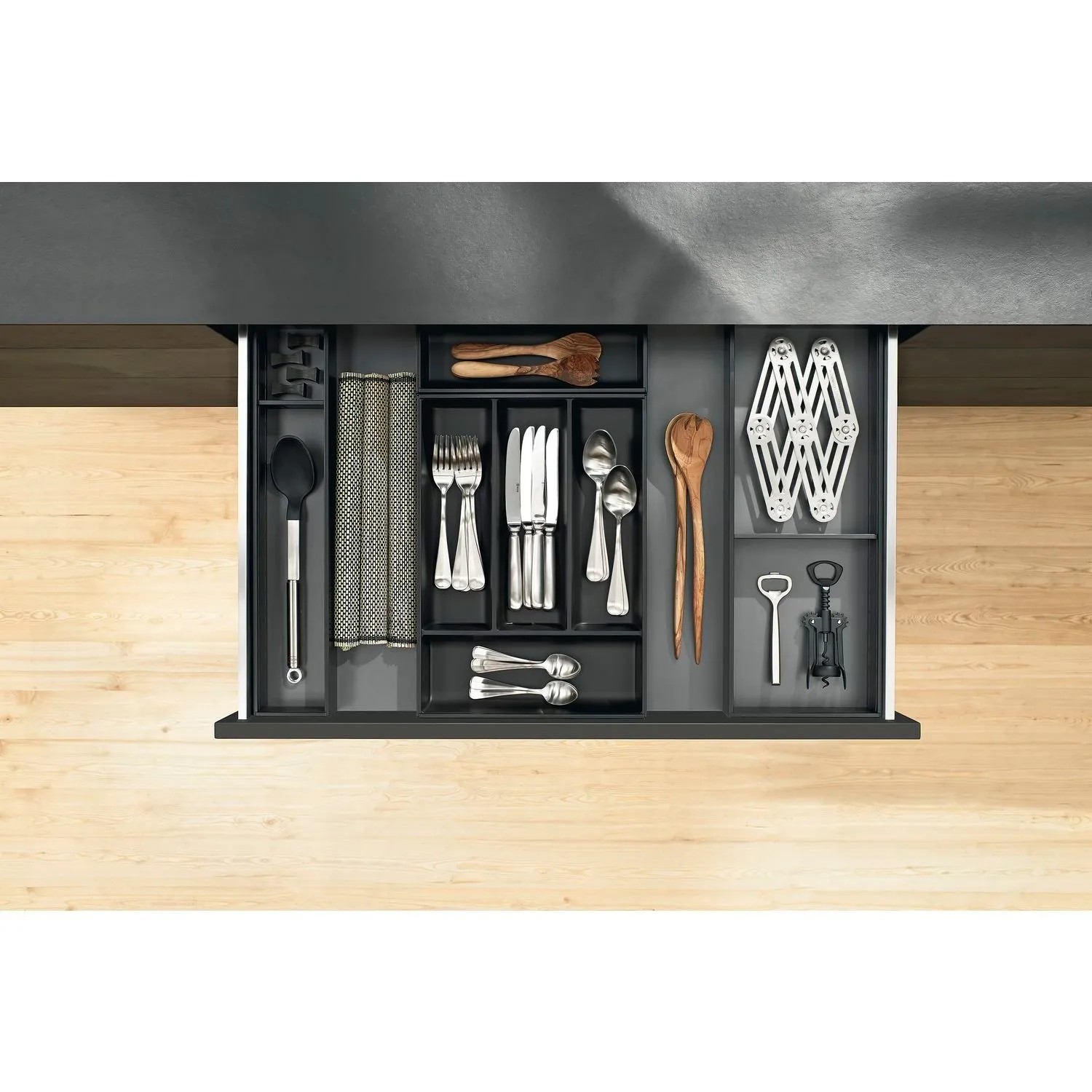 Blum Ambia-Line Schubladeneinsatz carbonschwarz im geöffneten Schubkasten, organisiert mit Besteck und Küchenhelfern.
