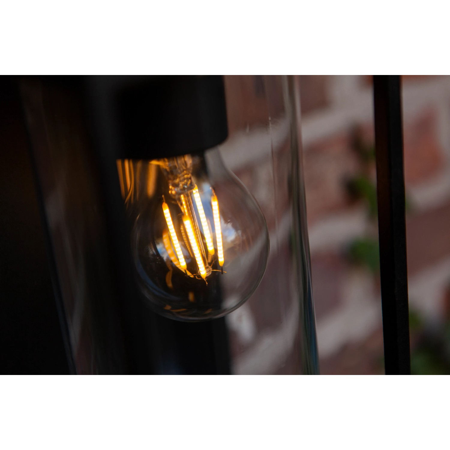 Schwarze, eckige Lutec Solar-Wandleuchte Flair mit klarem Zylinder und warmweißer Glühbirne.