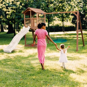 Axi Beach Tower Spielturm mit Nestschaukel und Rutsche im Garten mit Mutter und Kind.