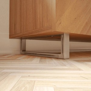 Zwei HEVVA Möbelfüße GRAZ aus Rohstahl-Klarlack, 10 cm hoch, unter einem Holzschrank auf Parkett.