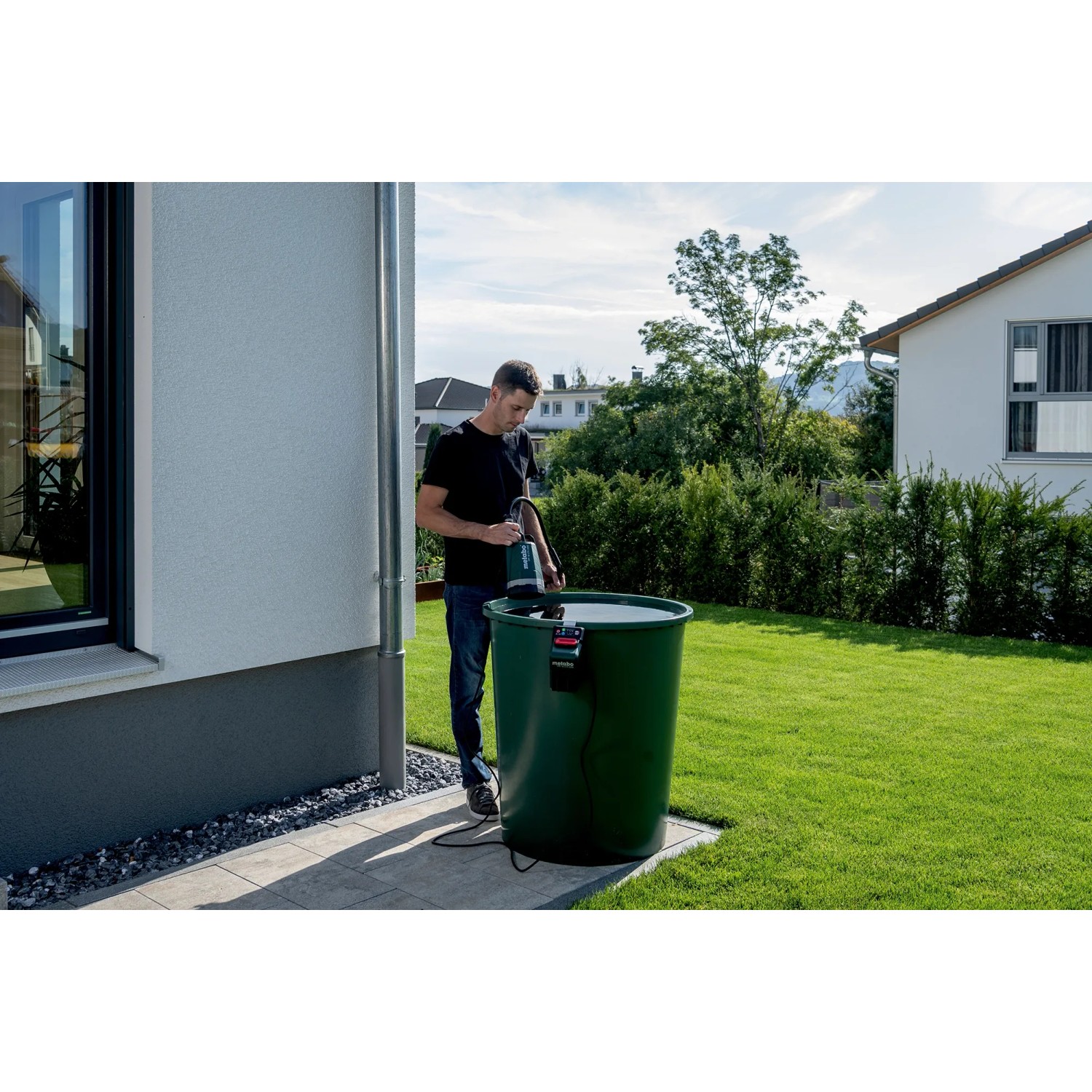 Mann nutzt Metabo Akku-Tauchpumpe TPF 18 LTX 2200 zur Gartenbewässerung aus Regentonne.