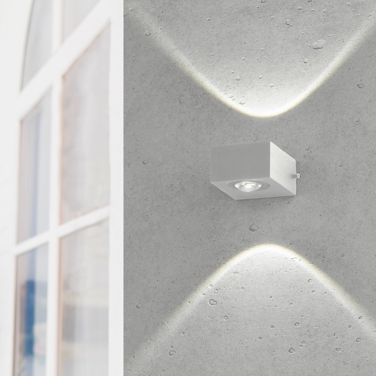 Silberne LED-Außenwandleuchte Helsinki von Fischer & Honsel mit warmweißem Licht an einer grauen Wand.