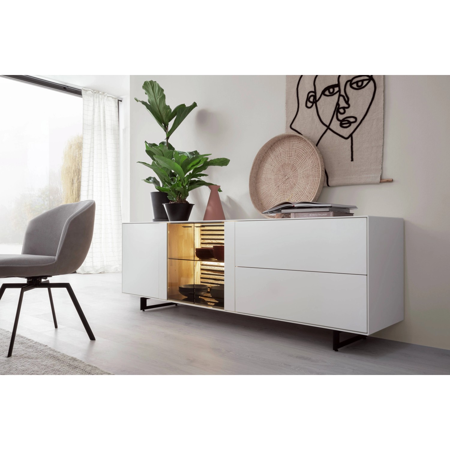 Modernes Sideboard in Weiß mit schwarzen Füßen, dekoriert mit Pflanzen und Wandbild.
