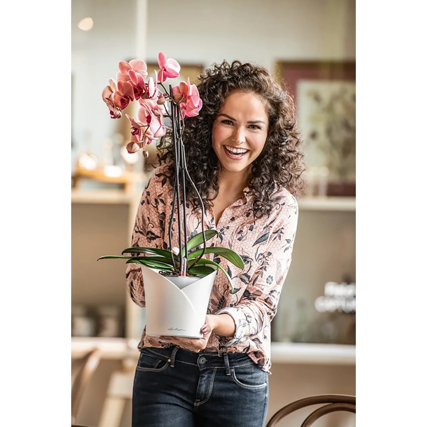 Frau hält weißen Lechuza Orchidea Pflanztopf mit rosa Orchidee. Ideal für Innenräume.