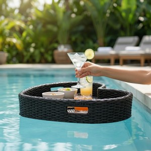 Schwarzes herzförmiges Schwimmtablett in Rattan-Optik schwimmt im Pool. Snacks und Cocktails darauf. Hand hält Glas. Poolzubehör.