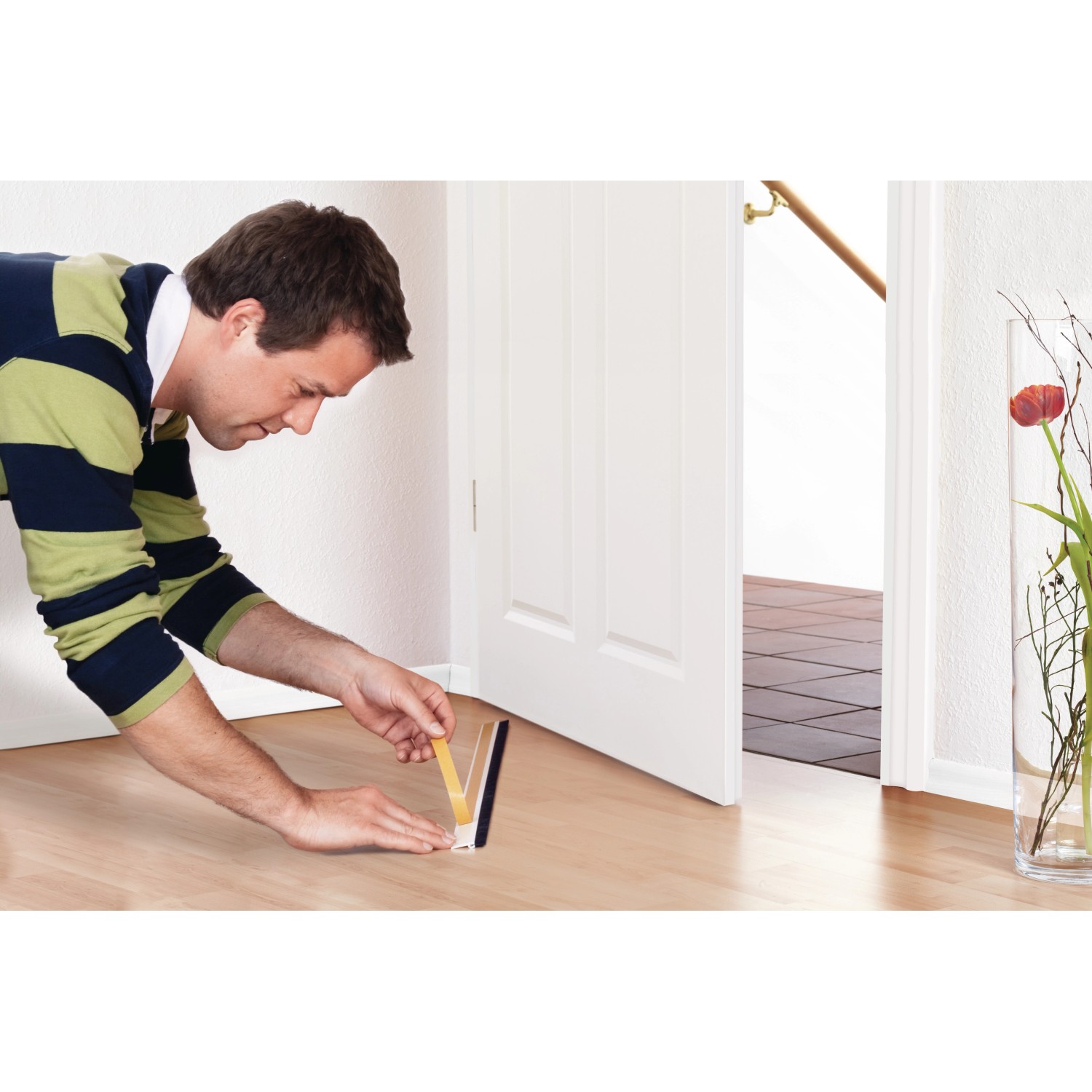 Mann befestigt weiße Tesamoll Türdichtschiene an Tür für unebene Böden.