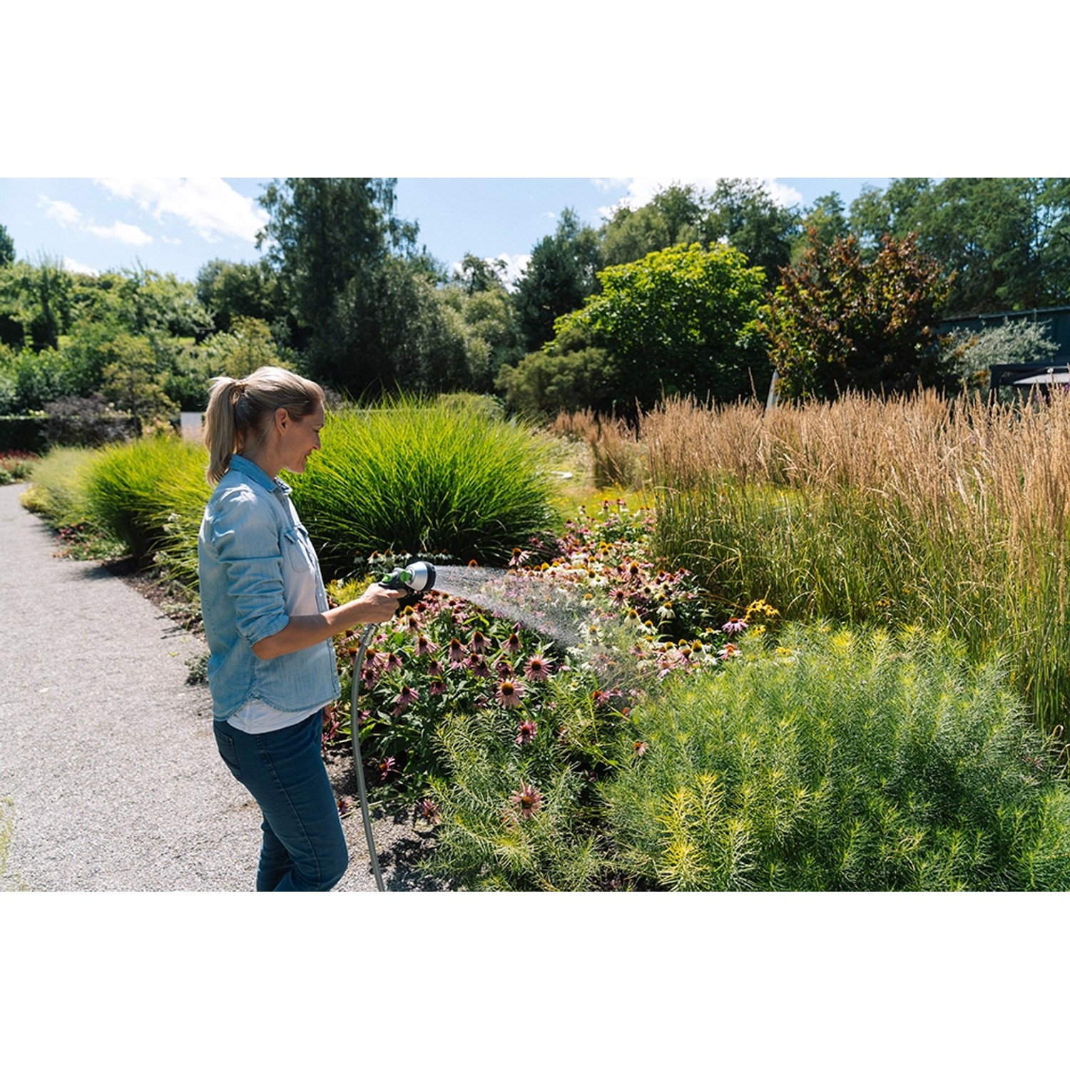 Frau bewässert Garten mit grauer Geka Multibrause Plus 3S Gartenspritze.