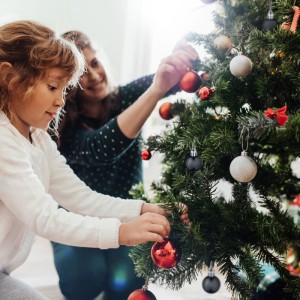 Schwarze Kunststoff-Weihnachtskugeln, matt und glänzend, am Tannenbaum. Kind und Erwachsene dekorieren festlich.