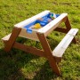 Axi Sand- und Wasser-Picknicktisch Nick, braunes Holz mit blauen Wannen und Sonnenschirm.