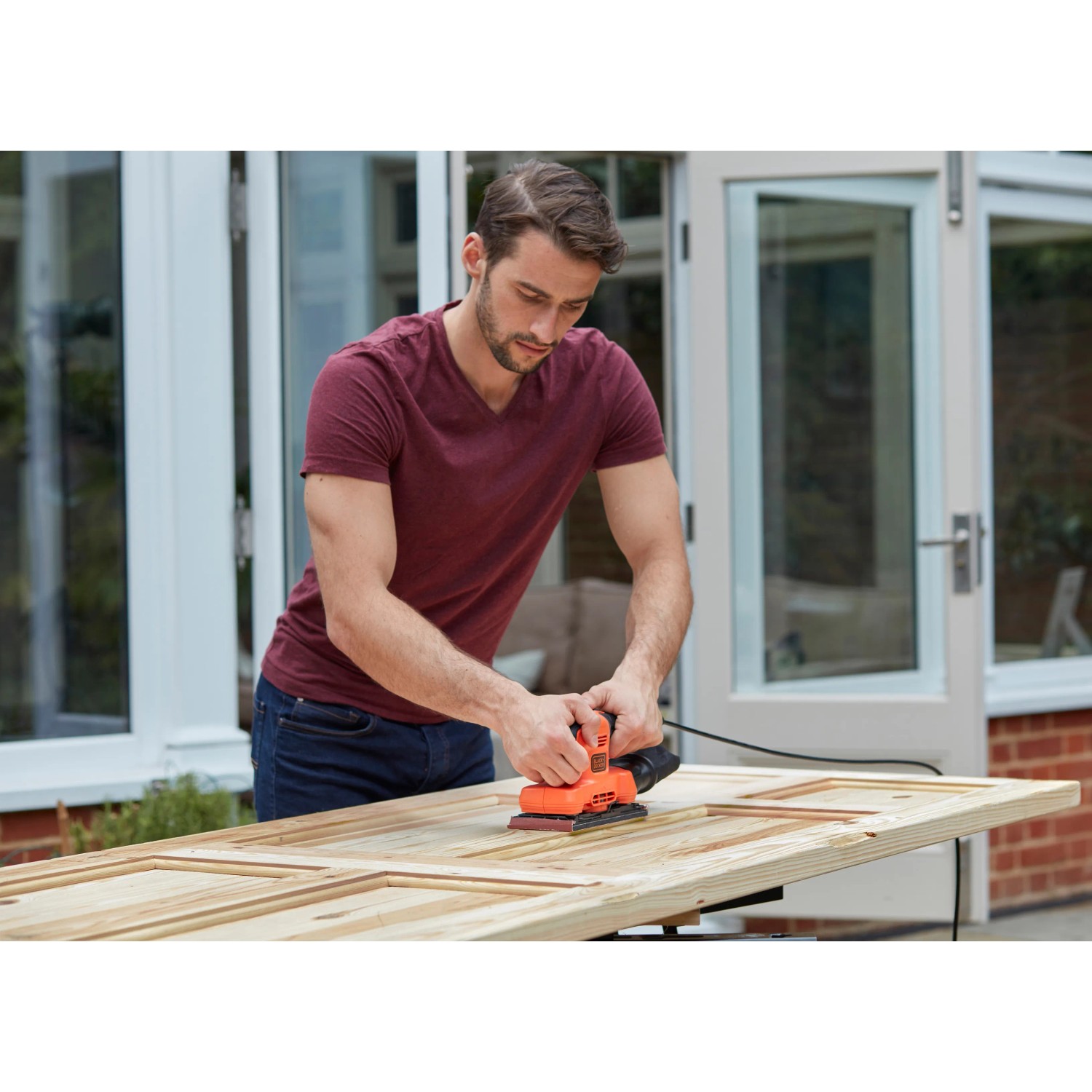 Mann schleift Holztür mit Black+Decker Schwingschleifer BEW220, 150 W. Schleifmaschine für Holzbearbeitung.