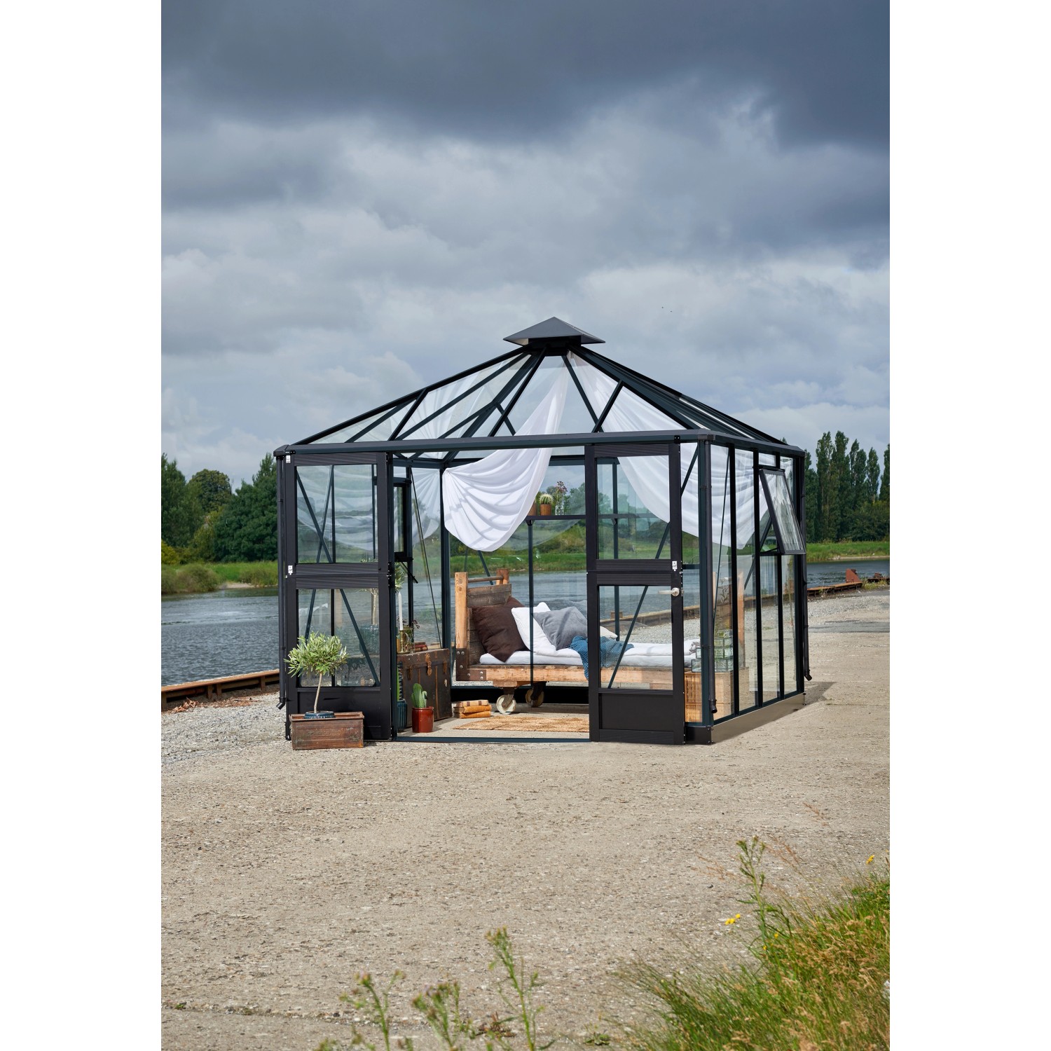 Juliana Gewächshaus Oase 8 Anthrazit mit Bett und Vorhängen. Begehbares Gewächshaus mit Glaswänden und anthrazitfarbenem Rahmen.