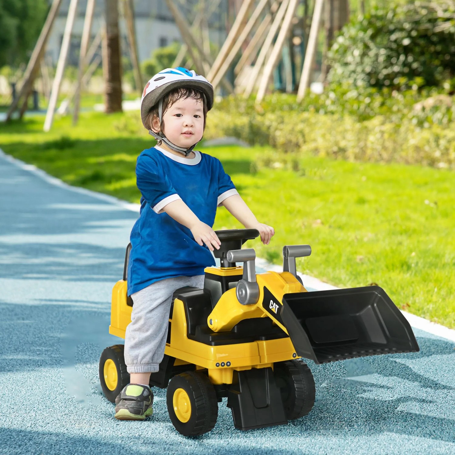 Kleinkind mit Helm fährt gelben HOMCOM Sitzbagger mit schwarzer Schaufel auf blauem Weg im Park.