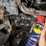 WD-40 Flexible Multifunktionsprodukt in Anwendung zur Autoreparatur. Schmiert schwer erreichbare Stellen.
