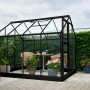 Schwarzes Halls Gewächshaus Popular 106 mit Pflanzen und Sitzgruppe im Garten.