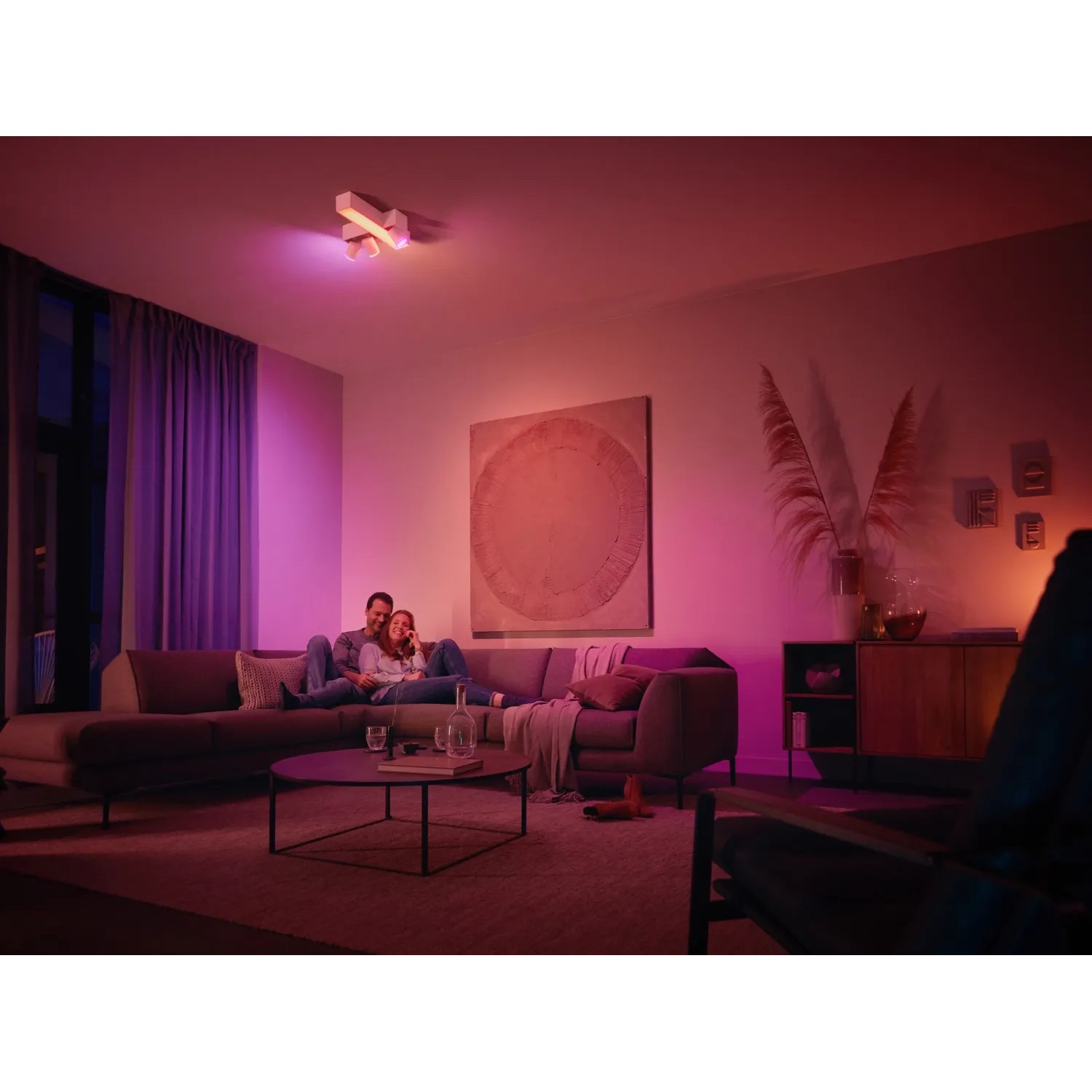 Philips Hue Centris Cross LED-Deckenleuchte mit 3 Spots in Weiß im Wohnzimmer mit farbiger Beleuchtung.