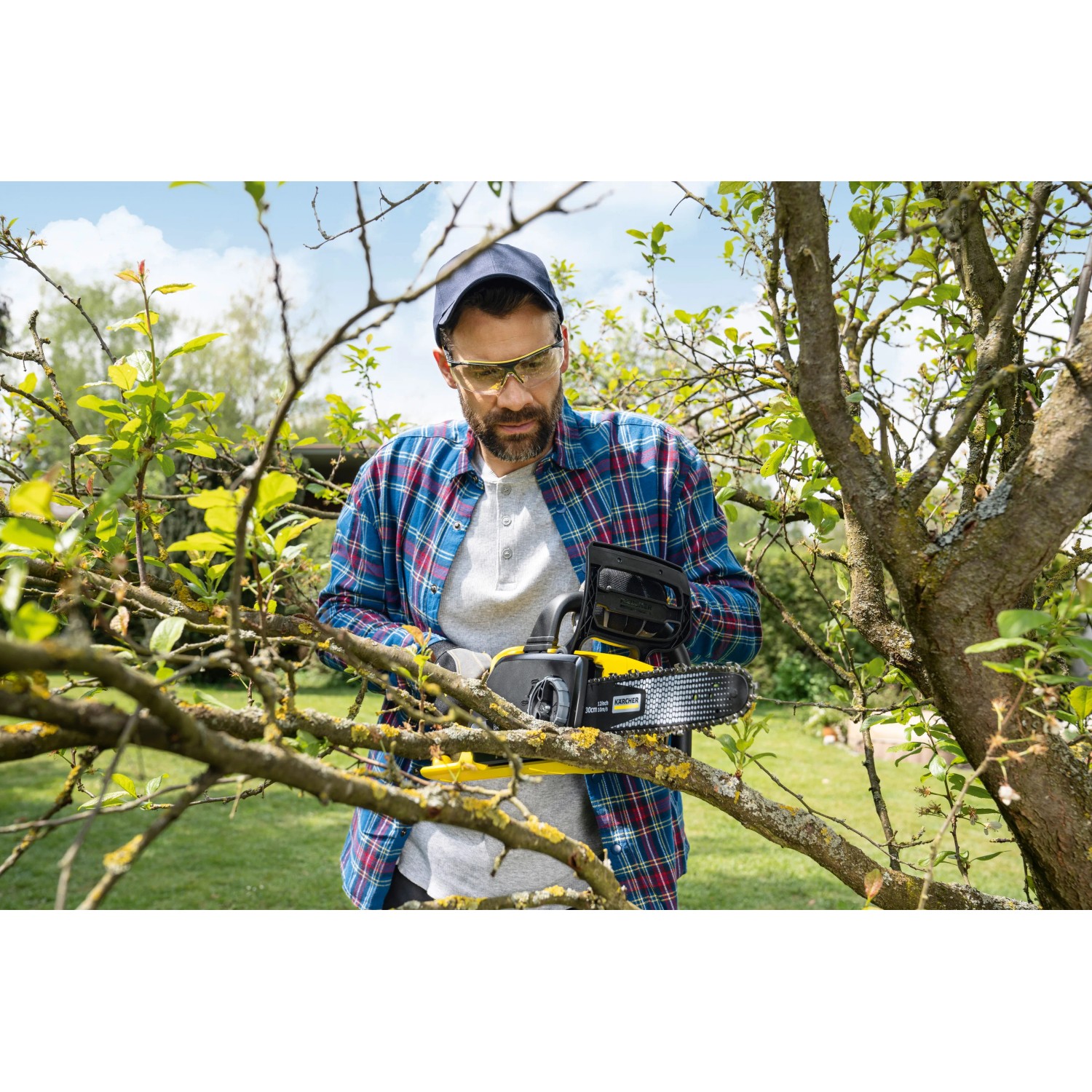 Mann arbeitet mit gelber Kärcher Akku-Kettensäge CNS 18-30 Battery an Baum im Garten.