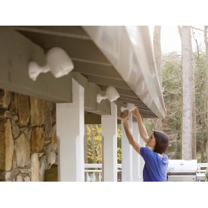 Frau montiert Mr. Beams LED-Außenstrahler mit Bewegungsmelder in Weiß an einer Hauswand.