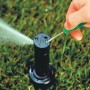 Rain Bird Versenkregner 32 SA im Einsatz: Einstellung mit Schraubenzieher, Wasserstrahl sichtbar.