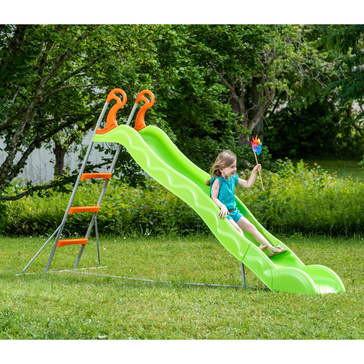 Grüne Trigano Rutsche Linou aus Metall mit Mädchen beim Rutschen im Garten.