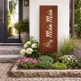 Rostbrauner Gartenstecker aus Eisen mit "Moin Moin" Schriftzug und Anker im Blumenbeet vor Hauseingang.