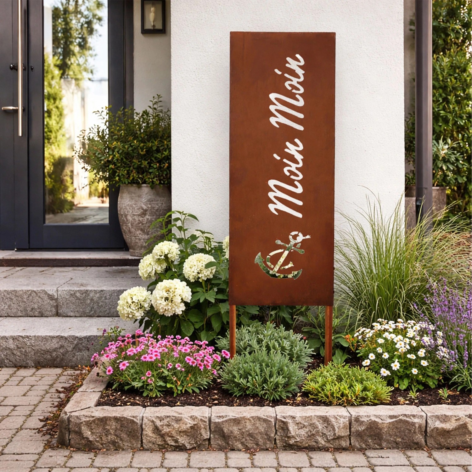Rostbrauner Gartenstecker aus Eisen mit "Moin Moin" Schriftzug und Anker im Blumenbeet vor Hauseingang.