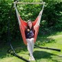 Orangefarbener AMANKA Hängesessel aus Baumwolle mit Holzstab, Frau sitzt entspannt im Garten auf schwarzem Gestell.