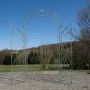 Antik-grüner Metall-Rosenbogen mit Tor als Rankhilfe im Garten. Dekorative Rankgitter für Kletterpflanzen.