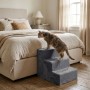 Graue 3-stufige Hundetreppe aus weichem Polyester neben einem Bett. Eine Katze nutzt die Aufstiegshilfe für Haustiere.