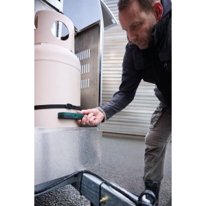 Mann prüft Gasfüllstand einer Gasflasche mit Bosch Filio Gas-Füllstandsprüfer. Grünes Ultraschall-Messgerät magnetisch an beiger Flasche.