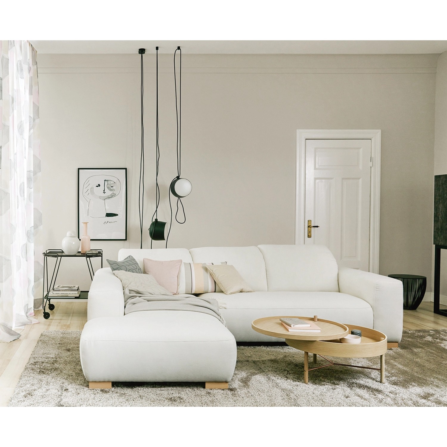 Wohnzimmer mit weißem Ecksofa, Couchtisch und Deko-Elementen vor einer hellen Wand.