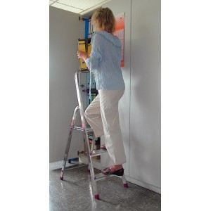 Krause Corda Stehleiter mit 3 Stufen im Einsatz: Frau steigt Leiter hoch, um Ordner ins Regal zu stellen.